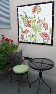 Photograph showing common courtyard area with artist designed poppy tile wall mural, patio furniture, and plants. 