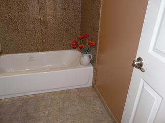 Photograph of bathroom showing speckled granite shower surround, white tub, tile floor, terracotta color painted walls, white panel door and brushed stainless hardware.